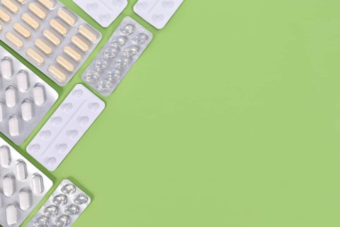 Different capsules and pills in blister packs on right side of green background with copy space,