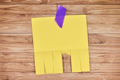 Yellow empty tear-off stub paper note without text on wooden wall,