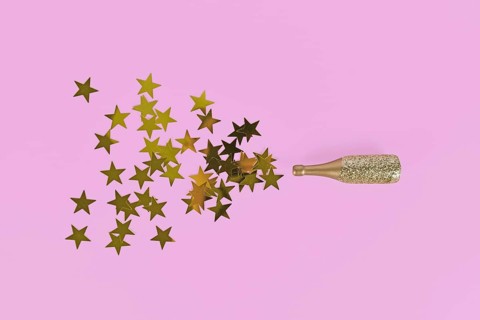 Golden star confetti splashing out of Champagne bottle on pink background,