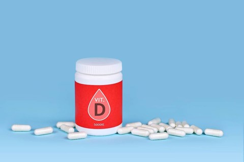 Vitamin D food supplement with container with pills on blue background,