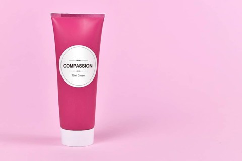 Compassion concept with cream tube with made up label saying Compassion, 75ml cream on pink background with blank copy space