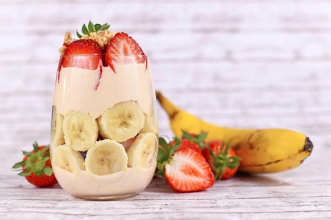 Healthy banana and strawberry fruit summer dessert with yogurt and granola layered in glass surrounded by fresh ingredients,