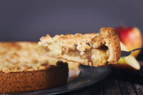Single slice of traditional European apple pie with topping crumbles on cake server,