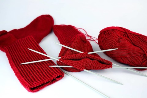 Self-knitted red socks made of wool isolated against a white background with knitting needle and ball of wool,