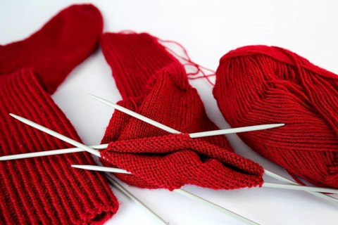 Self-knitted red socks made of wool isolated against a white background with knitting needle and ball of wool,