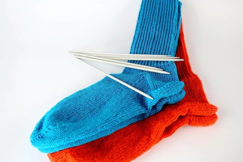 Self-knitted socks made of wool isolated against a white background in orange and blue with knitting needle and ball of wool,