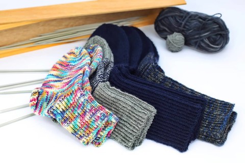 Self-knitted socks made of wool isolated against a white background. In different colours and sizes. With knitting needle and ball of wool,