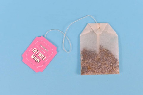 Tea bag with made up cute pink label with text Get well soon on pastel blue background,