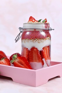 Strawberry fruit dessert with yogurt, healthy chia seeds and puffed quinoa grains layered in jar surrounded by berries on pink wooden tray