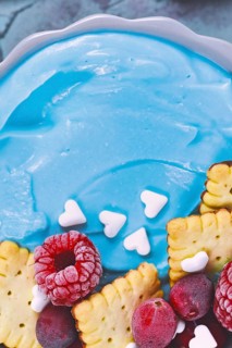 Detail shot of healthy fruit smoothie bowl dyed blue with natural spirulina powder and topped with red raspberry and cranberry and small biscuits,