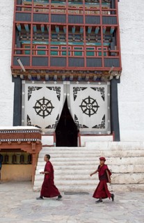 Two novices walk across the monastery courtyard, the entrance portal at the back