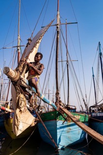 Man sitting on the yard of a fishing boat in the Arab quarter, repairing the square sail