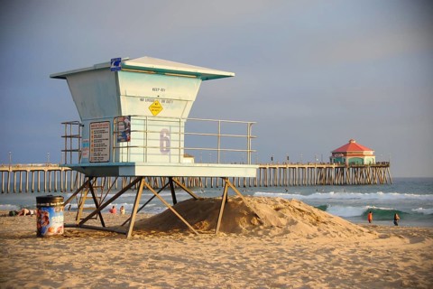 A lifeguard tower on a californian beach at sunset. Far behind is Huntington Beach Pier,