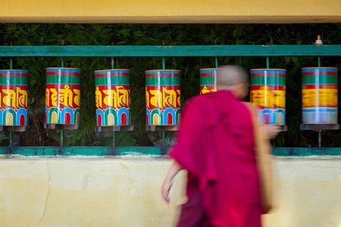 Buddhist monk passing and rotating prayer wheels on kora around Tsuglagkhang complex in McLeod Ganj