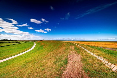 View from the dike in Greetsiel towards Pilsum in the Pilsum lighthouse in summer with scattered clouds
