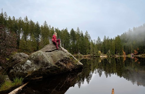Woman in red on rocks in Glaswaldsee surrounded by forest
