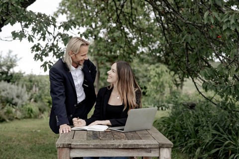 Businessman and businesswoman working in the open on a laptop at a wooden table