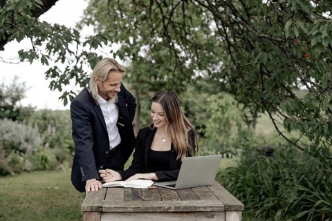 Businessman and businesswoman working in the open on a laptop at a wooden table