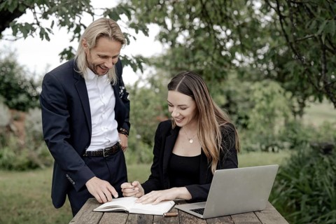 Businessman and businesswoman working in the open on a laptop at a wooden table