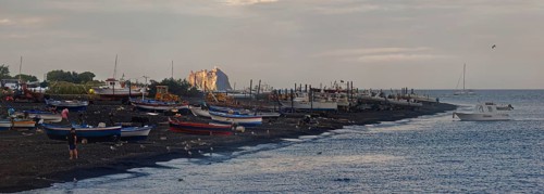 Boats on the sandy beach of San Vincenzo the volcano and Stromboli island at sunset