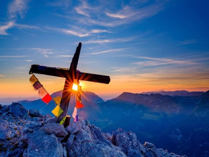 Buddhist prayer flags at the summit cross of the Kleiner Watzmann at sunrise