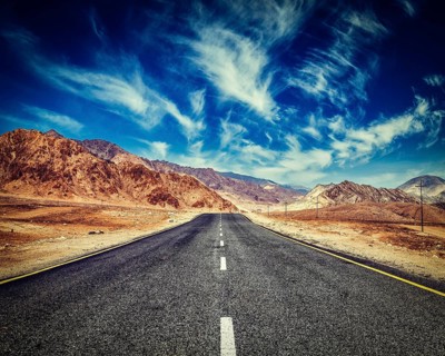 Vintage retro effect filtered hipster style image of road in mountains Himalayas and dramatic clouds on blue sky. Ladakh