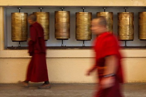 Buddhist monk passing and rotating prayer wheels on kora around Tsuglagkhang complex in McLeod Ganj