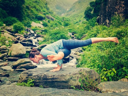 Vintage retro effect hipster style image of sporty fit woman doing yoga asana Eka Pada Koundinyasana 1 at tropical waterfall