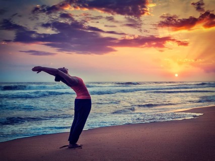 Vintage retro effect hipster style image of young sporty fit woman doing yoga Sun salutation Surya Namaskar pose Hasta Uttanasana on tropical beach on sunset