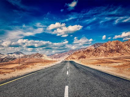 Vintage retro effect filtered hipster style image of road in mountains Himalayas and dramatic clouds on blue sky. Ladakh