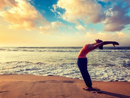 Vintage retro effect hipster style image of young sporty fit woman doing yoga Sun salutation Surya Namaskar pose Hasta Uttanasana on tropical beach on sunset