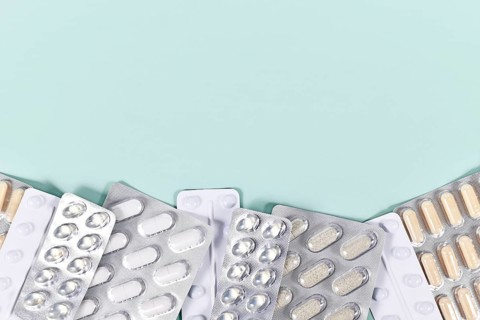 Blister packs with various pills and capsules at bottom of mint green background with copy space