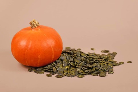 Green pumpkin seeds next to whole 'Red Kuri Hokkaido' squash