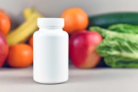 Food nutrition supplement bottle in front of fruits and vegetables in blurry background