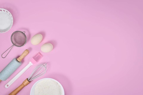 Cake dough ingredients and baking tools on pink background with copy space
