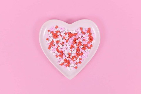 Plate with heart shaped sugar sprinkles on pink background
