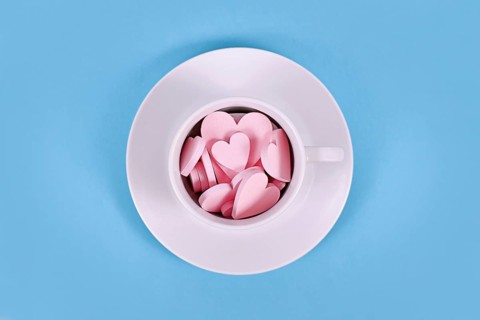 Pink wooden heart ornaments in white tea cup on blue background