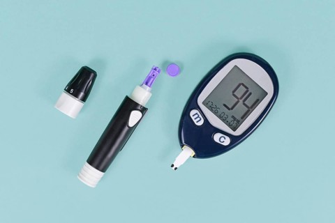Tools for diabetes treatment with blood glucose sugar meter showing blood sugar of 94 and lancing device with lancet on blue background
