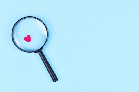 Looking for love concept with magnifier glass and pink heart icon on blue background with copy space