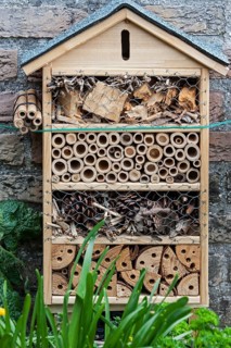 Insect hotel with artificial nesting facilities for solitary bees and burrows for hibernating ladybirds and butterflies near flower and vegetable garden