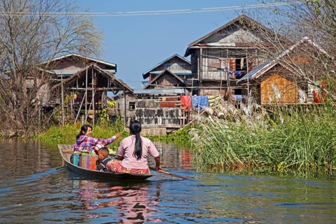 Intha woman with child in proa row to lake village with traditional wooden houses on stilts in Inle Lake