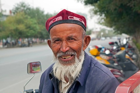 Close-up of an elderly Uighur man with a beard wearing a doppa in Qiemo