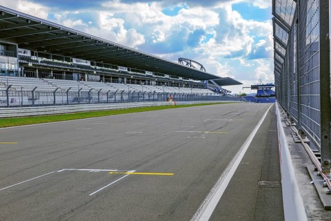 View through security fence from pit lane to empty start-finish straight grid lane with markings for start position