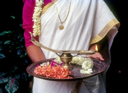 A girl holding oil lamp and flowers on a tray during Onam festival