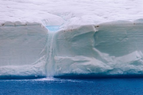 Meltwater flowing from the ice wall of the melting Brasvellbreen Glacier into the Arctic Ocean