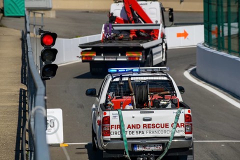 Tow truck and rescue vehicle drive through exit from pit lane onto race track at red lights due to race stoppage