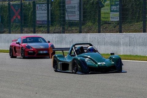 Radical SR10 open-wheel racing car in front behind Porsche Cayman GT4 races at high speed top speed during trackday on start-finish straight of race track