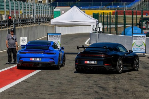 Two Porsche GT3 sports cars waiting at red lights at pit lane exit for clearance to enter race track