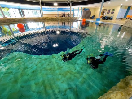 Pair of divers diving swimming close under water surface in clear water from indoor diving tower