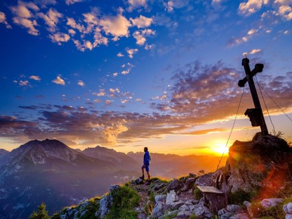Mountaineer standing at sunset at the summit cross of the Brettgabel